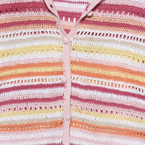 Pu&ograve; includere: Primo piano di un cardigan all'uncinetto colorato. Il maglione presenta strisce orizzontali nelle tonalit&agrave; del rosa, bianco, giallo e arancione. Ha una chiusura con bottoni sul davanti e un colletto e finiture rosa chiaro. L'uncinetto ha un design aperto e arioso.