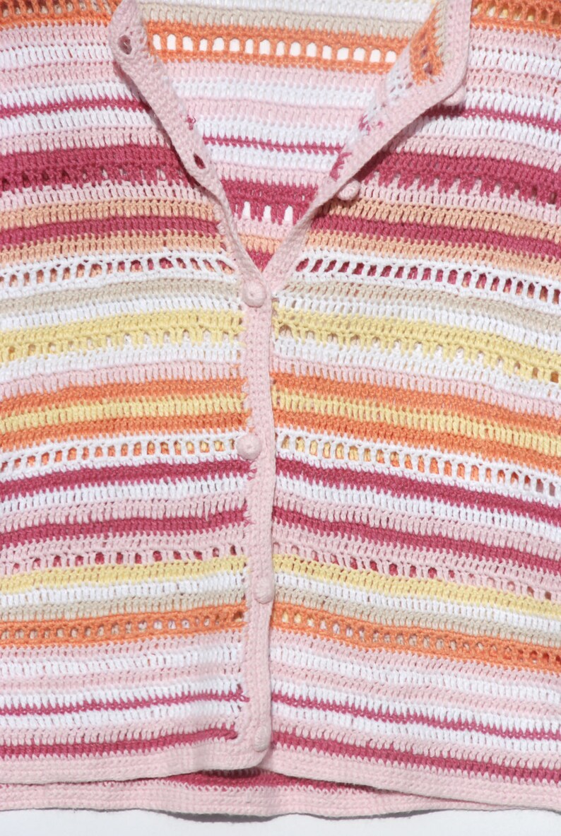 Pu&ograve; includere: Primo piano di un cardigan all'uncinetto colorato. Il maglione presenta strisce orizzontali nelle tonalit&agrave; del rosa, bianco, giallo e arancione. Ha una chiusura con bottoni sul davanti e un colletto e finiture rosa chiaro. L'uncinetto ha un design aperto e arioso.