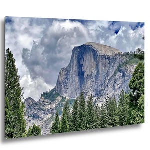 May include: A landscape photograph of Half Dome in Yosemite National Park, featuring the iconic granite rock formation rising above a dense forest of green pine trees under a sky filled with large, dramatic white and grey clouds.