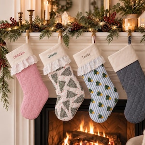 Puede incluir: Cuatro calcetines navideños acolchados colgados en fila. El primero es rosa con el nombre Christina, el segundo es blanco con árboles verdes y el nombre Jessie, el tercero es de rayas azules con árboles y el nombre Teddy, y el cuarto es azul marino.