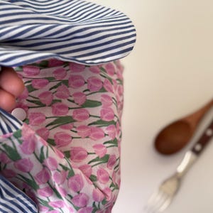 May include: A close-up of a fabric item with a blue and white striped pattern, and a pink floral pattern. A wooden spoon and fork are in the background.