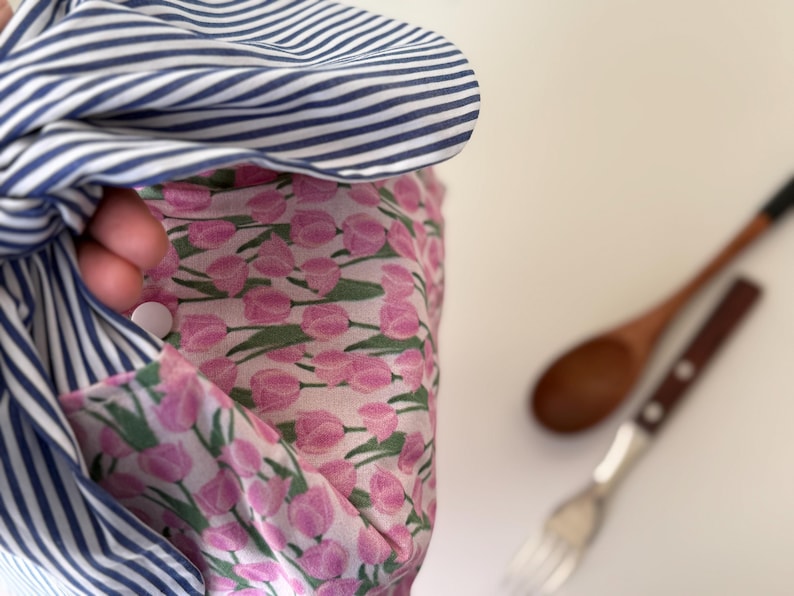 May include: A close-up of a fabric item with a blue and white striped pattern, and a pink floral pattern. A wooden spoon and fork are in the background.