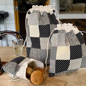 May include: Three drawstring bags made of patchwork fabric featuring a black, white, and gray color palette. The patterns include polka dots, stripes, gingham, and small floral prints. The bags have white fabric tops with white drawstring cords.