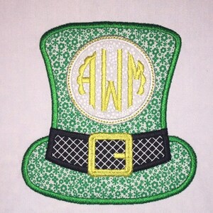May include: Green and gold embroidered leprechaun hat with a white circle and the monogram "AWM" in gold. The hat has a black and gold belt.