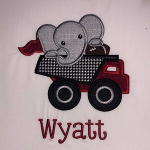 May include: Embroidered design of a red truck with a gray elephant and a football in the bed. The truck has black tires and a black and white checkered pattern on the bed. The text "Wyatt" is embroidered below the truck.