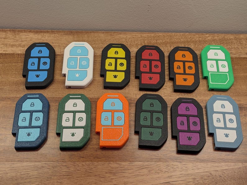 Puede incluir: Doce fundas rectangulares para llaves dispuestas en dos filas. Cada funda presenta una disposici&oacute;n de cinco botones con iconos de bloqueo, desbloqueo, encendido y alarma. Las fundas vienen en varios colores s&oacute;lidos, incluyendo azul, blanco, amarillo, rojo, naranja, verde, azul oscuro, turquesa y morado.