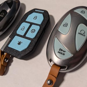 Puede incluir: Tres mandos de coche. Uno es plateado con botones negros, otro es negro con botones azul claro y otro es plateado con botones azul claro. Dos de los mandos cuentan con correas de cuero marr&oacute;n con remaches met&aacute;licos plateados.