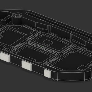 Puede incluir: Una carcasa electr&oacute;nica de pl&aacute;stico negro con un interior rebajado, compartimentos rectangulares y un inserto de metal roscado. Cuatro botones peque&ntilde;os, cuadrados y de color claro est&aacute;n situados a lo largo del borde lateral curvo.