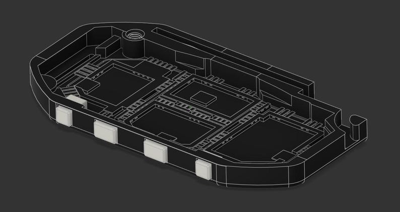 Puede incluir: Una carcasa electr&oacute;nica de pl&aacute;stico negro con un interior rebajado, compartimentos rectangulares y un inserto de metal roscado. Cuatro botones peque&ntilde;os, cuadrados y de color claro est&aacute;n situados a lo largo del borde lateral curvo.