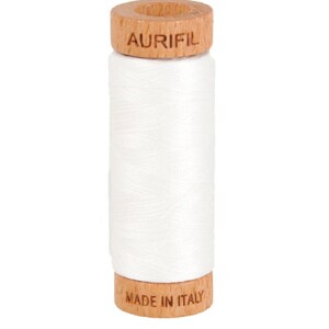 May include: A white spool of Aurifil thread. The thread is tightly wound around a central core. The wooden top and bottom of the spool are stamped with the brand name and "MADE IN ITALY".