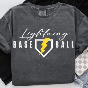 May include: Dark gray sweatshirt with the words "Lightning Baseball" in white script and block letters. A yellow lightning bolt is inside a white home plate graphic. The sweatshirt has a crew neck and long sleeves.