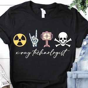 May include: Black t-shirt with a graphic design featuring a yellow radiation symbol, a skeleton hand, an X-ray machine, and a skull with crossbones. The words "x-ray technologist" are written in cursive below the graphics.