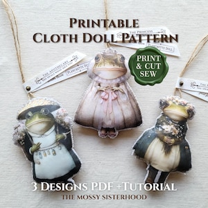 May include: Three printed cloth doll ornaments featuring anthropomorphic frogs dressed in vintage-style clothing. The dolls are suspended by twine and include labels with text such as PRINTABLE CLOTH DOLL PATTERN, THE APOTHECARY, and PRINT & CUT SEW.