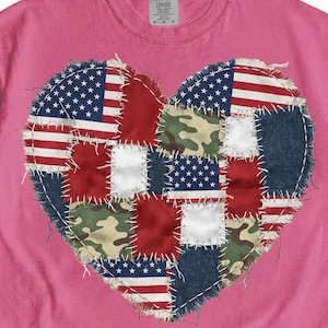 以下が含まれることがあります： ピンク色のTシャツ。ハート型のパッチワークデザインが特徴です。ハートは、アメリカ国旗、迷彩柄、デニムなど、さまざまな生地の正方形で構成されています。ハートの縁は白い糸で縫い付けられており、テクスチャード加工が施されています。
