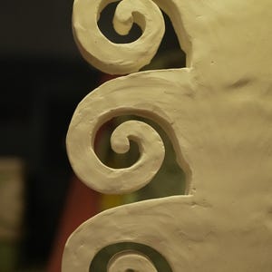 May include: Close-up of a cream-coloured, sculpted architectural element featuring a series of spiral designs. The swirls are rounded and smooth, with a matte finish. The background is blurred, highlighting the texture and form of the sculpture.
