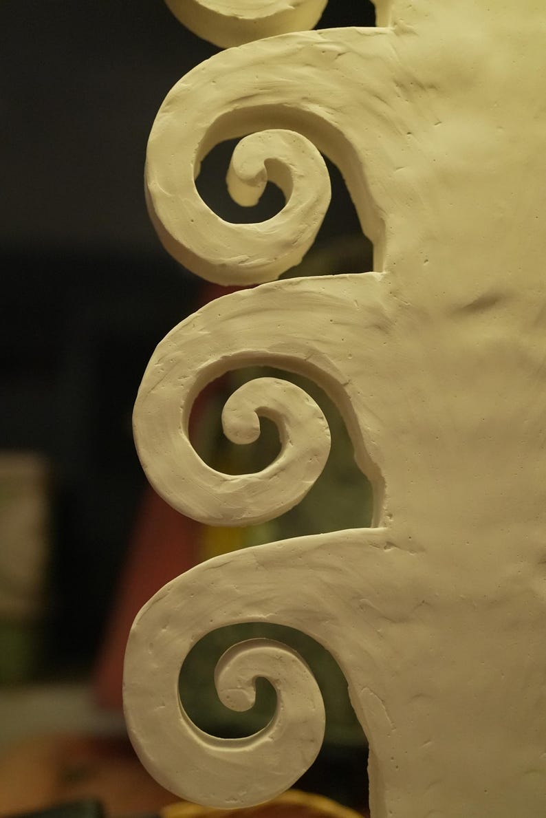 May include: Close-up of a cream-coloured, sculpted architectural element featuring a series of spiral designs. The swirls are rounded and smooth, with a matte finish. The background is blurred, highlighting the texture and form of the sculpture.