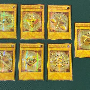 May include: Seven gold-colored trading cards with holographic designs. Each card features a unique symbol within a circular pattern, with Japanese text at the top. The cards are rectangular with rounded corners and a gold border.