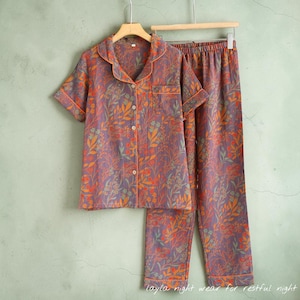 May include: A two-piece pajama set with a floral pattern in shades of purple, orange, and green. The short-sleeved button-down shirt and pants are hanging on a wooden hanger. The text "layla night wear for restful night" is at the bottom.
