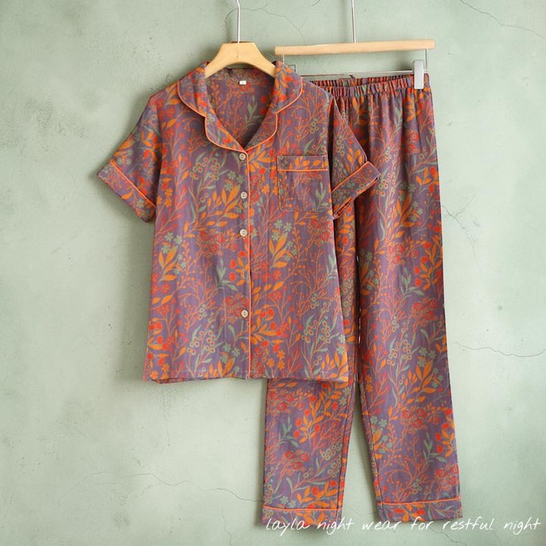 May include: A two-piece pajama set with a floral pattern in shades of purple, orange, and green. The short-sleeved button-down shirt and pants are hanging on a wooden hanger. The text "layla night wear for restful night" is at the bottom.