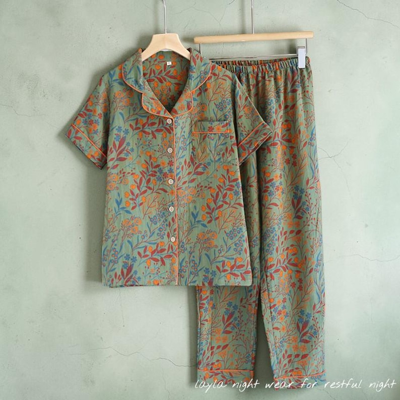 May include: A two-piece pajama set with a floral pattern in shades of green, orange, and blue. The short-sleeved top has a button-down front and a notched collar. The pants are long and have a matching floral design. The text "layla night wear for restful night" is at the bottom.