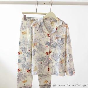 May include: Cream-coloured pyjama set with a floral pattern in blue, red, and yellow. The long-sleeved top has a collared neckline and button-down front. The pyjama trousers have an elastic waistband. The text at the bottom says "night wear for restful night".