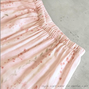 May include: Close-up of pink pajama bottoms with an elastic waistband. The fabric is patterned with small red flowers and green leaves. The text "layla night wear for restful night" is printed on the bottom right corner.