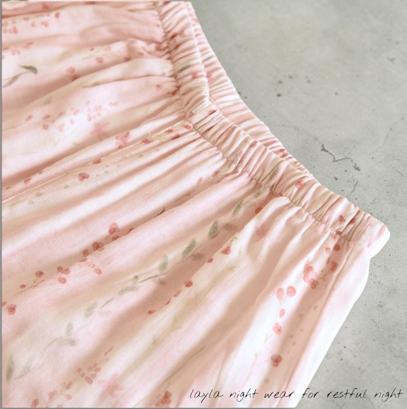 May include: Close-up of pink pajama bottoms with an elastic waistband. The fabric is patterned with small red flowers and green leaves. The text "layla night wear for restful night" is printed on the bottom right corner.