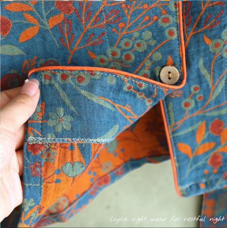 May include: Close-up of a teal pajama top with an orange floral pattern and orange trim. The fabric is quilted and has a button closure. The text "Layla night wear for restful night" is visible at the bottom.