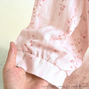 May include: A light pink pajama sleeve with a floral pattern and a gathered cuff. The fabric has a delicate print of small, reddish-pink flowers and leaves. The text "layla night wear for restful night" is visible at the bottom.