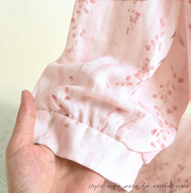 May include: A light pink pajama sleeve with a floral pattern and a gathered cuff. The fabric has a delicate print of small, reddish-pink flowers and leaves. The text "layla night wear for restful night" is visible at the bottom.