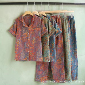 May include: A set of floral-patterned pajamas in shades of purple, orange, and green, hanging on wooden hangers. The short-sleeved top has a button-down front and a notched collar. The matching pants are long. The text "Layla night wear for restful night" is at the bottom.
