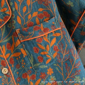 May include: Close-up of a teal pajama top with an orange floral pattern. The top has a breast pocket with orange trim and a wooden button. The text "Layla night wear for restful night" is at the bottom.