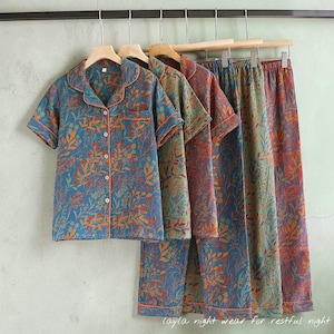 May include: Several sets of floral-patterned pajamas hang on wooden hangers. The short-sleeved tops and pants feature a blue background with orange and green botanical designs. The pajamas have orange trim and are made of a soft fabric.
