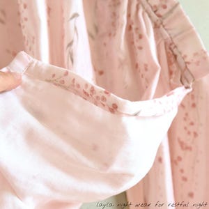 May include: Close-up of a light pink pajama top with a floral pattern. The inside of the sleeve is visible, showing a contrasting floral print. The text "layla night wear for restful night" is at the bottom.