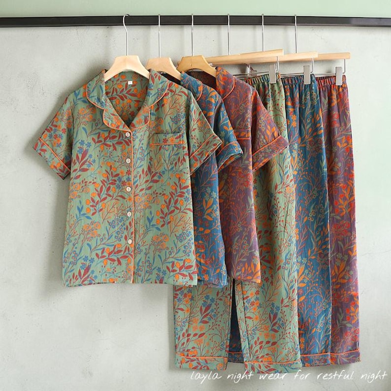 May include: A collection of floral-patterned pajama sets in shades of green, blue, and purple, hanging on wooden hangers. Each set includes a short-sleeved button-up shirt and matching pants. The text "layla night wear for restful night" is visible at the bottom.