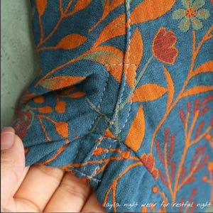 May include: Close-up of teal fabric with an orange floral pattern. The fabric is stitched together with white thread. The text "layla night wear for restful night" is visible in the bottom right corner.