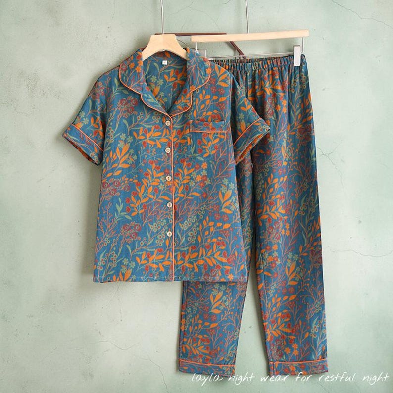 May include: Blue pajama set with a floral pattern in orange and red. The short-sleeved top has a button-down front and a chest pocket. The pants are long and straight-legged. The set is trimmed with orange piping. Text at the bottom reads: layla night wear for restful night.