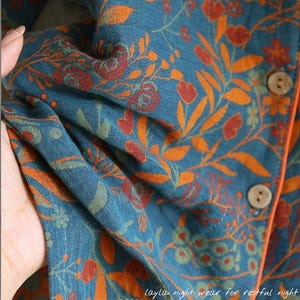 May include: Close-up of teal fabric with an orange floral pattern. The fabric is part of a garment, with visible buttons and orange trim. The text "Layla night wear for restful night" is at the bottom.