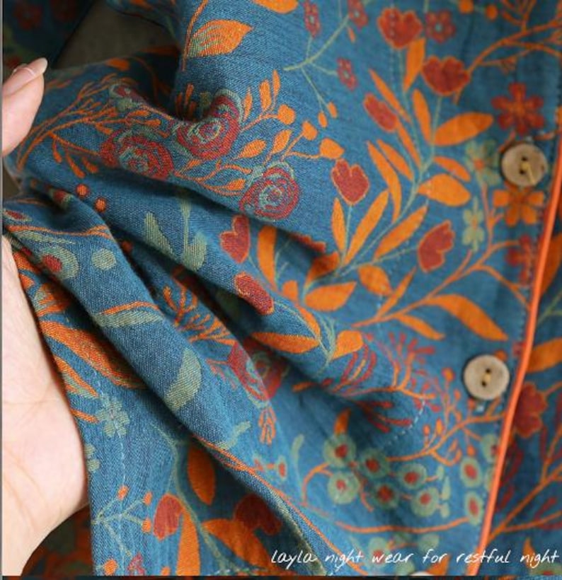 May include: Close-up of teal fabric with an orange floral pattern. The fabric is part of a garment, with visible buttons and orange trim. The text "Layla night wear for restful night" is at the bottom.