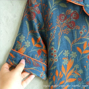 May include: Blue pajama top with a floral pattern in orange, red, and green. The short-sleeved top has orange trim and the text "layla night wear for restful night" at the bottom.