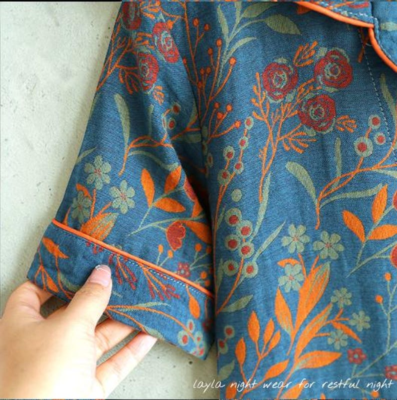 May include: Blue pajama top with a floral pattern in orange, red, and green. The short-sleeved top has orange trim and the text "layla night wear for restful night" at the bottom.