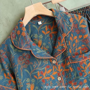 May include: Close-up of a teal pajama set with an orange floral pattern. The set includes a button-down shirt with an orange trim and a pocket. The text "Layla night wear for restful night" is visible at the bottom.