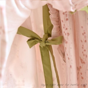 May include: Close-up of a light pink nightgown with a green bow. The nightgown has a floral pattern and the text "layla night wear for restful night" at the bottom. The fabric appears soft and delicate.