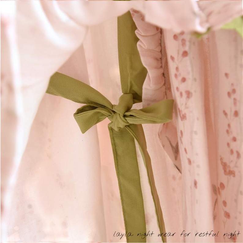 May include: Close-up of a light pink nightgown with a green bow. The nightgown has a floral pattern and the text "layla night wear for restful night" at the bottom. The fabric appears soft and delicate.