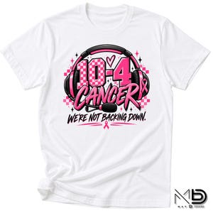 Könnte beinhalten: Ein weißes T-Shirt mit einer Grafik aus schwarzen Kopfhörern, die den Text 10-4 CANCER umgeben. Das Design enthält rosa Akzente, ein Karomuster und den Text WE'RE NOT BACKING DOWN mit einem kleinen rosa Schleifensymbol unter dem Schriftzug.