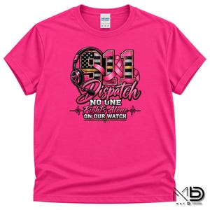 May include: A bright pink short-sleeved t-shirt featuring a graphic design with a headset, the number 911, and a pink ribbon. The text reads 911 Dispatch, No One Fights Alone, and On Our Watch, with a heart icon and a heartbeat line graphic.