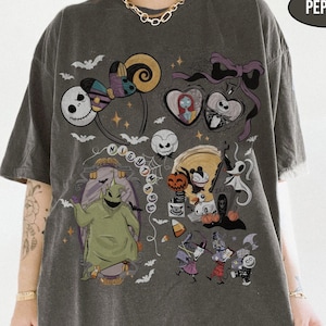 May include: Dark gray t-shirt featuring a colorful graphic design with characters and elements from the movie "The Nightmare Before Christmas." The design includes Jack Skellington, Sally, Oogie Boogie, and other iconic imagery. The word "NIGHTMARE" is also visible.