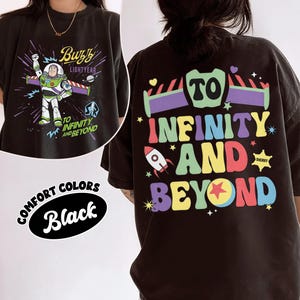 Op de afbeelding: Zwart T-shirt met een Buzz Lightyear-afbeelding op de voorkant en de tekst "To Infinity and Beyond" op de achterkant. De afbeelding op de voorkant toont Buzz Lightyear in zijn ruimtepak. De afbeelding op de achterkant heeft een raket en kleurrijke tekst.