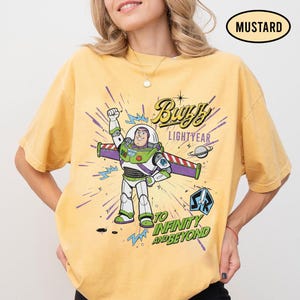 May include: Mustard-colored t-shirt featuring a graphic of Buzz Lightyear from Toy Story. The design includes the words "Buzz Lightyear" and "To Infinity and Beyond." The shirt has short sleeves and a crew neck.