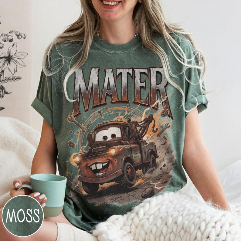 Puede incluir: Camiseta verde con una imagen de dibujos animados de Mate de la pel&iacute;cula Cars. El gr&aacute;fico incluye el nombre "MATER" encima del personaje. La camiseta tiene un aspecto vintage y desgastado.
